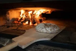 Feuer im Holzofen mit Brot im Hintergrund